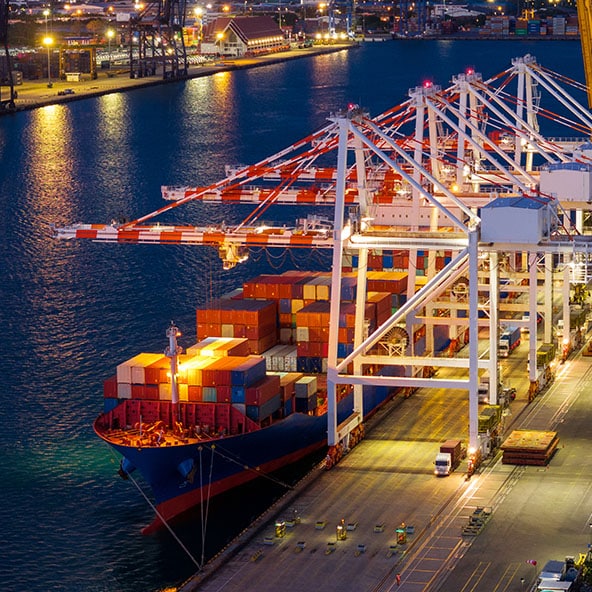 Crane loading cargo container from trucks to container ship at a port terminal.