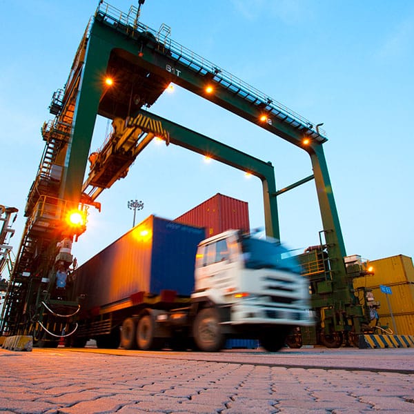Blurred motion of truck with cargo containers and cranes in a shipping port.
