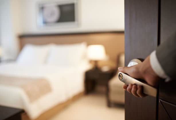 Hand opening the door to a neatly appointed hotel room.