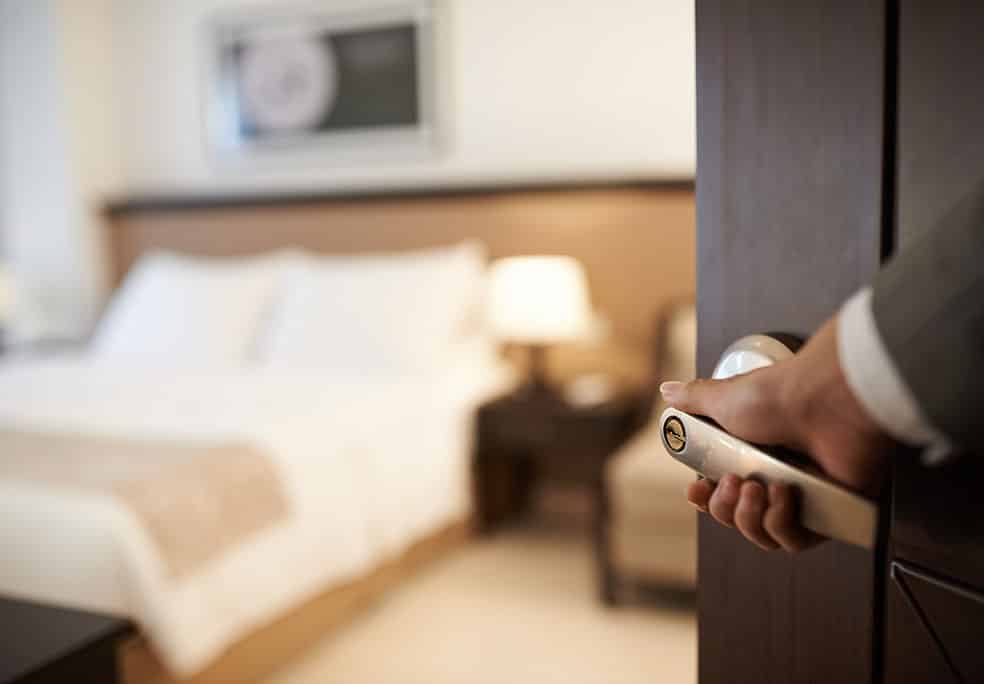 Hand opening the door to a neatly appointed hotel room.
