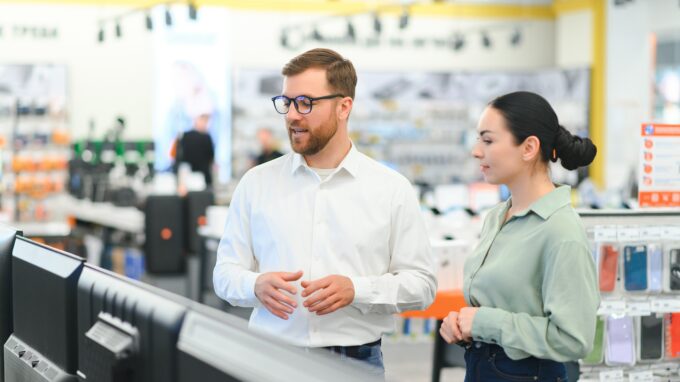 Young woman choosing tv set with shop assistant in home appliance shopping mall supermarket.