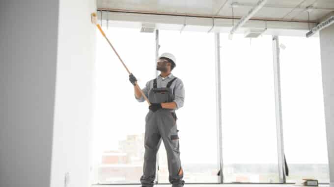 man paints a white wall in a commercial space with a roller. Repair of the interior.