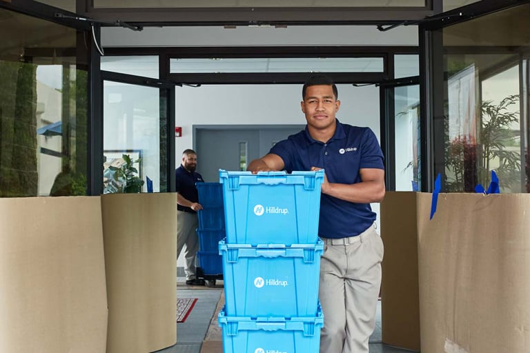 Hilldrup team rolling stacks of totes out of a workplace with floor and door protection in place. 