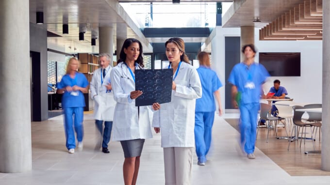 Two Female Doctors In White Coats Discussing Patient Scan In Busy Hospital