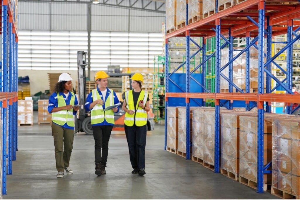 Three individuals walking through a warehouse wearing reflective vests.