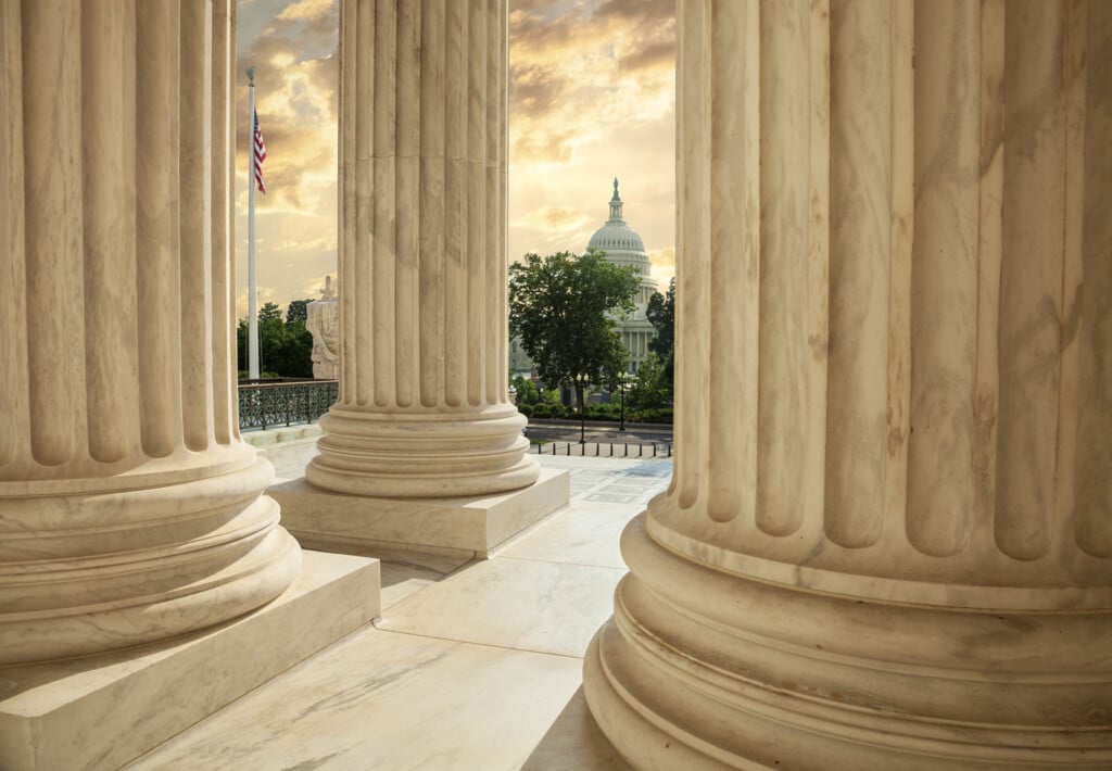 United States Capitol Building viewed between columns of the Supreme Court at sunset